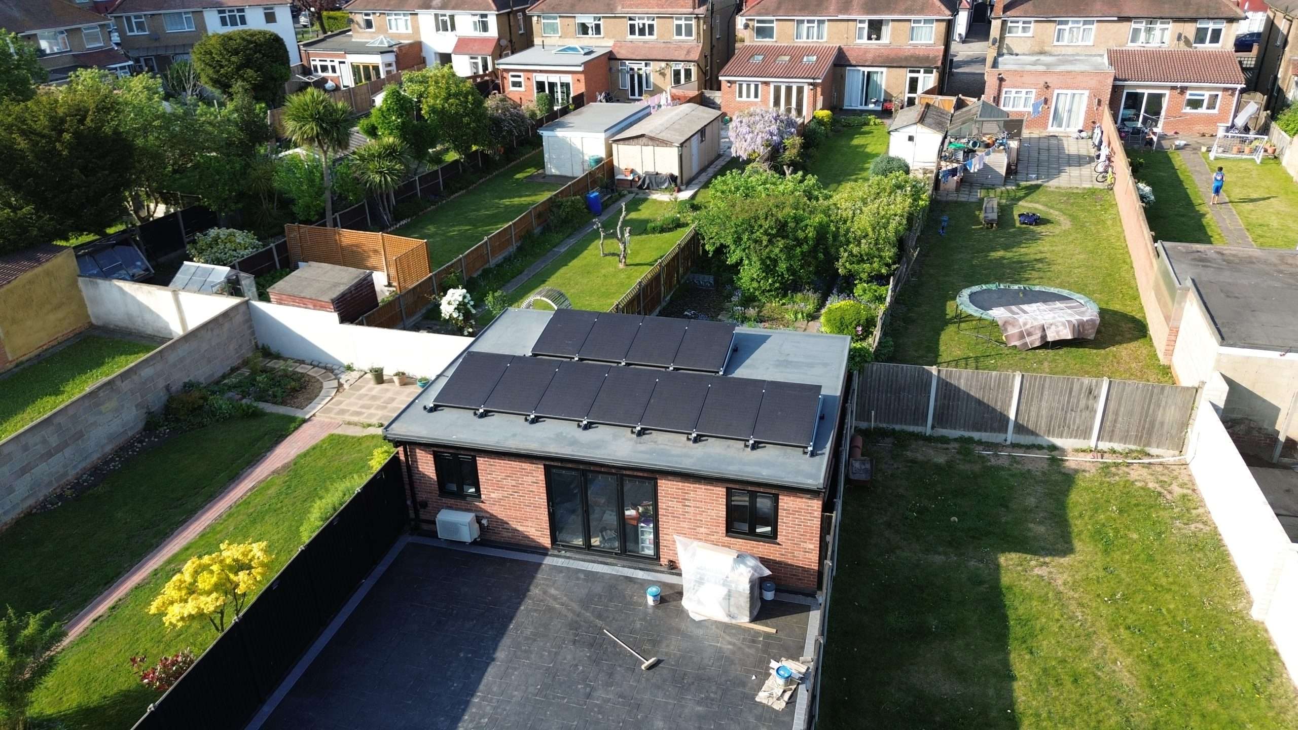 Aerial view of a residential extension with solar panels on a flat roof, surrounded by back gardens.